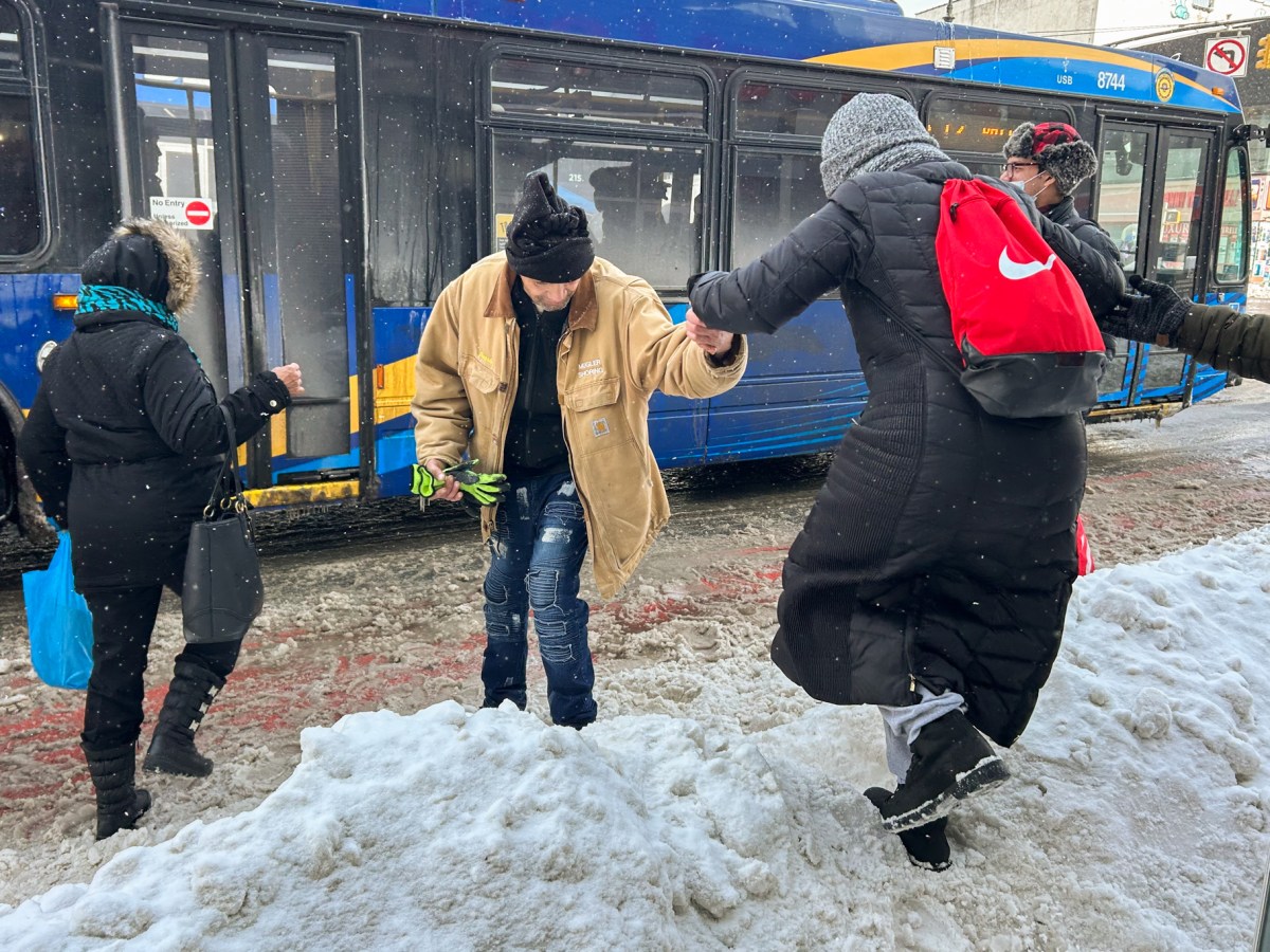 Arnaldo Duarte helps another commuter over a snowbank trying to board a bus on Fordham Road in The Bronx,