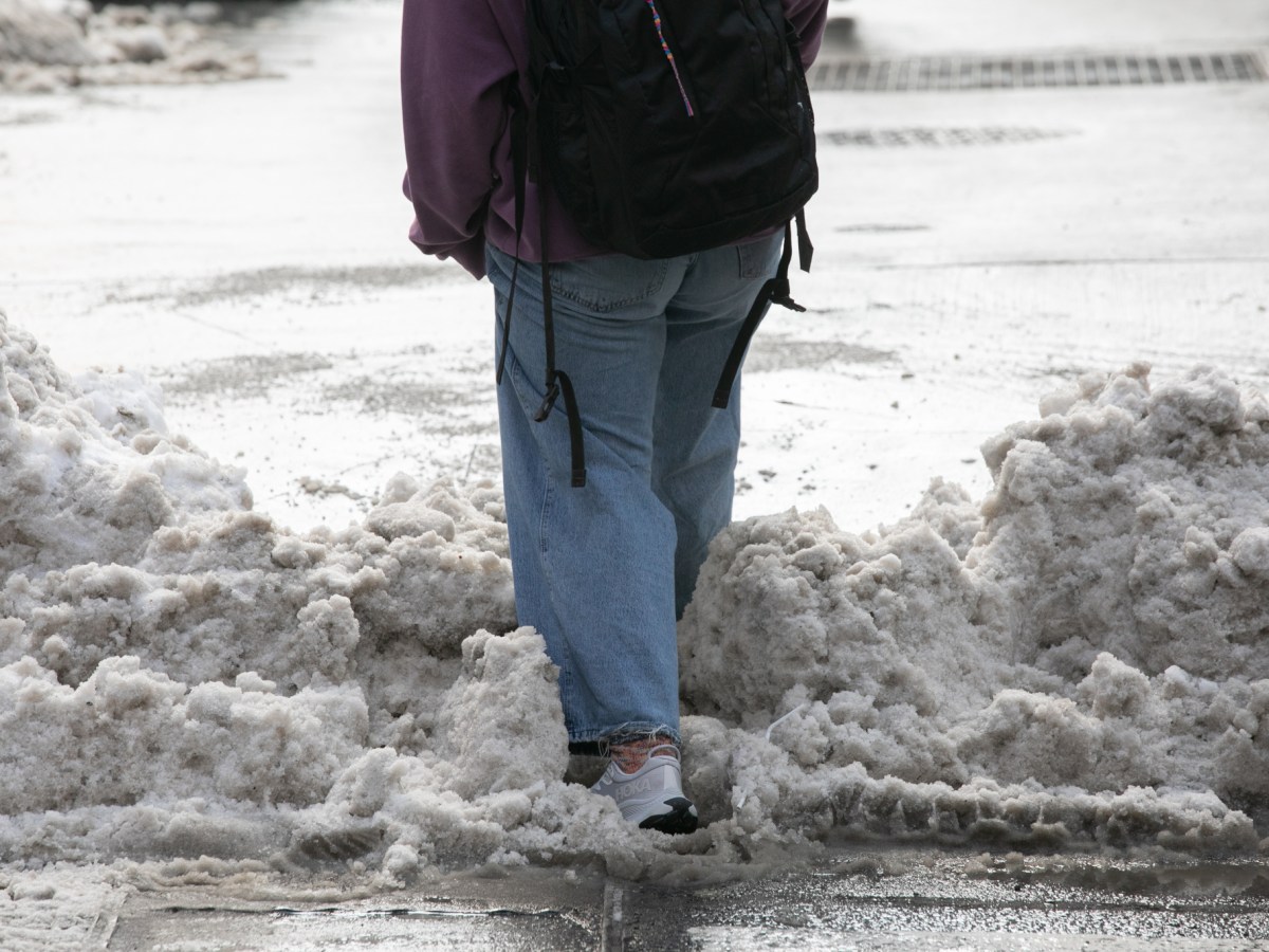 A pedestrian in Lower Manhattan navigates an unshoveled intersection