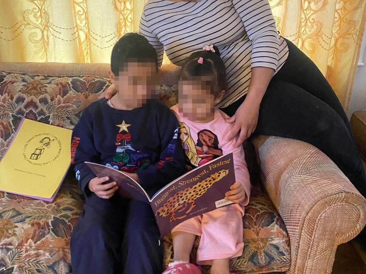 Ingrid holds her two young children while they read on a couch.